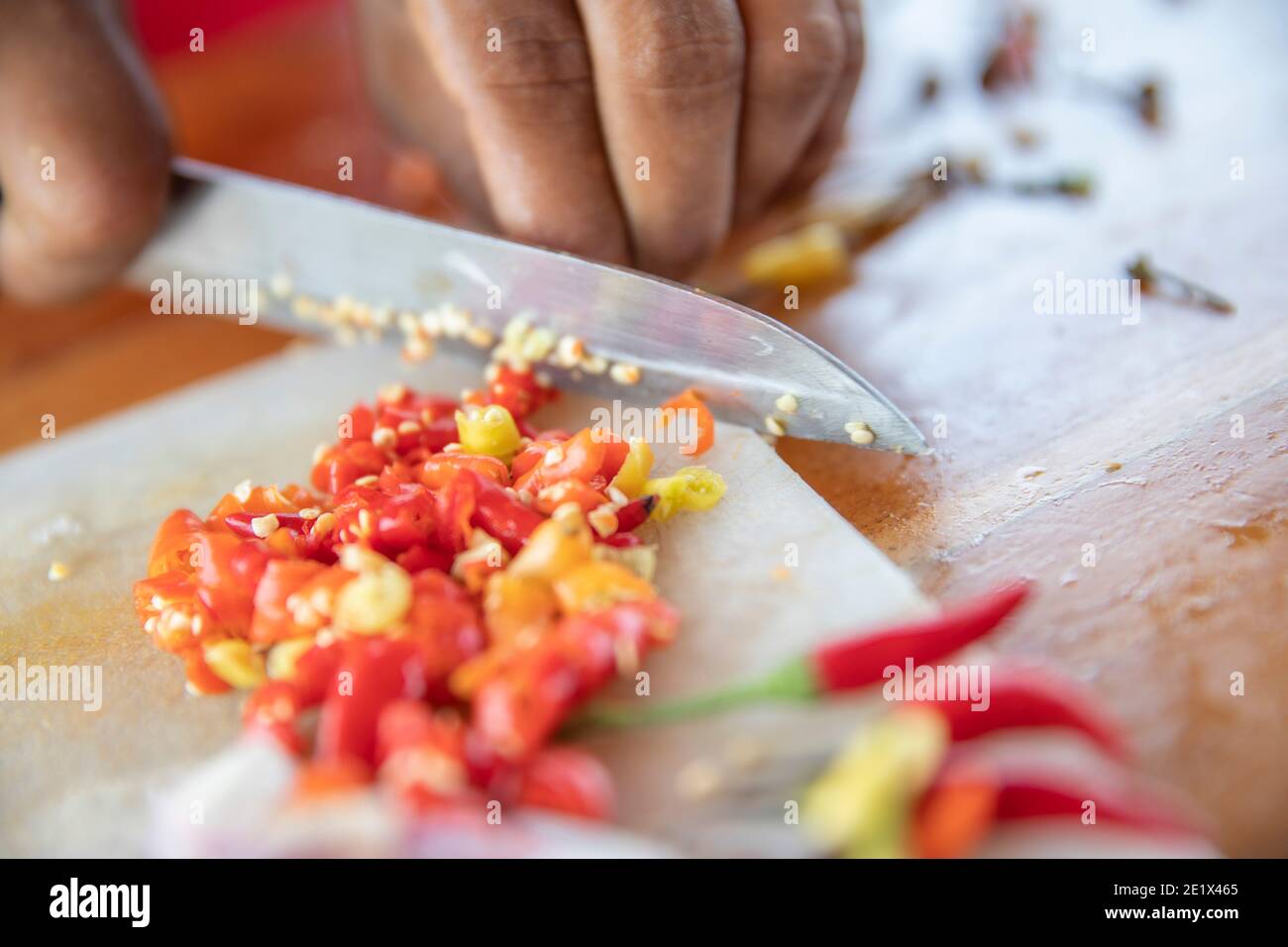 close up of a hand cutting white onions and chilli pepper on a kitchen board with a knife Stock Photo