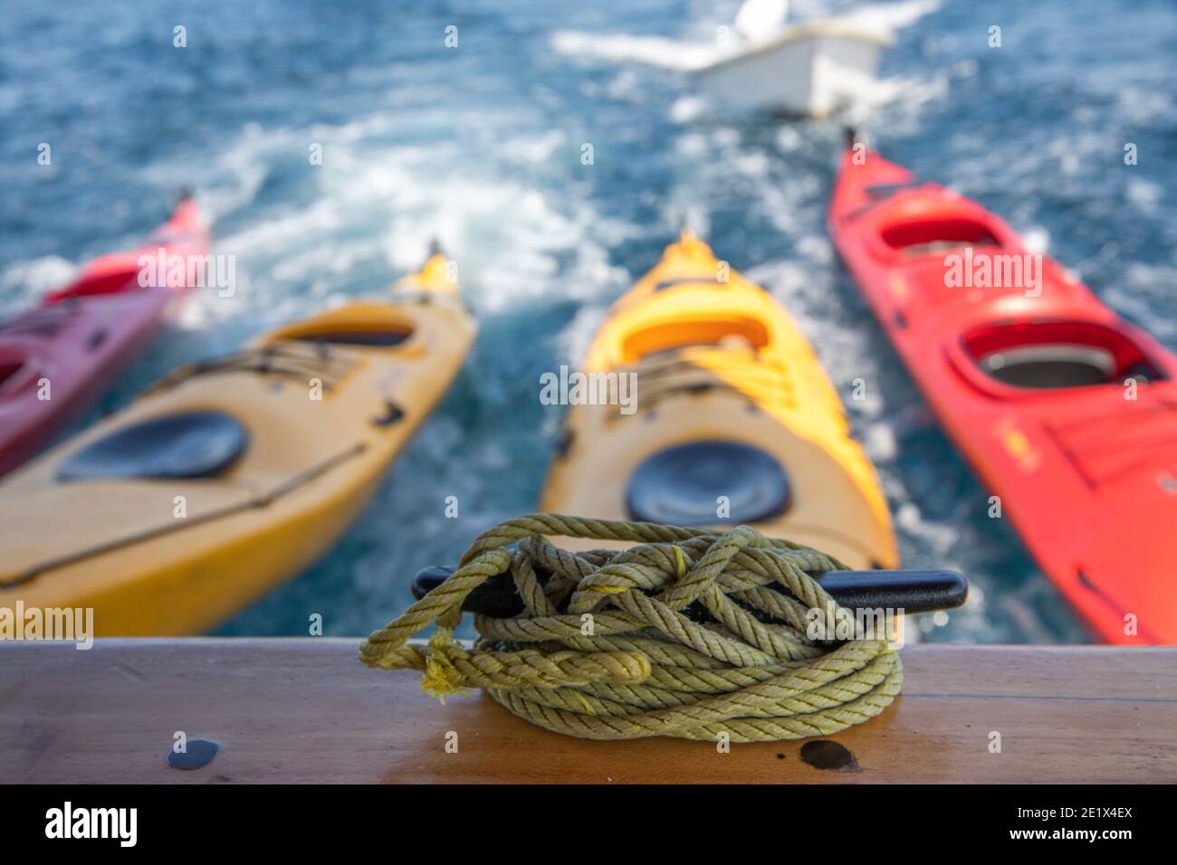 colorful Kayaks bound together towed by a ship and some sailing ropes in the foreground Stock Photo
