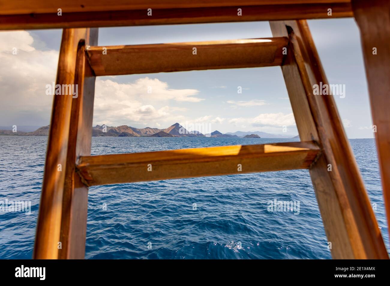 panoramic views out from a wooden cruise ship into turquoise water and an island range at the horizon in Komodo National Marine Park Stock Photo