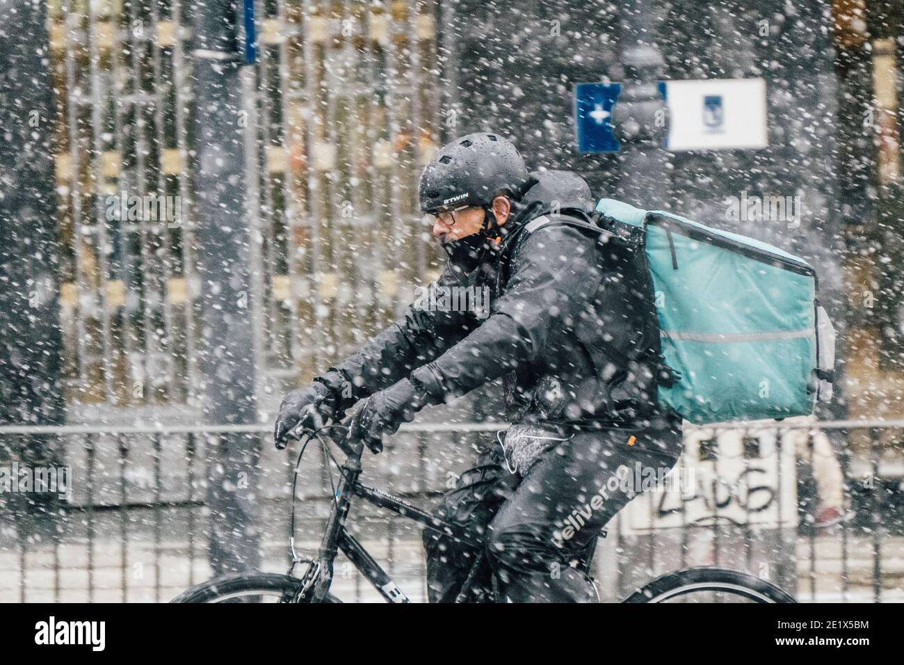 Madrid, Spain - January 2021: Deliveroo (food delivery company) rider in Alacala street with hevy snow due to Filomena Storm. Picture from the left, r Stock Photo