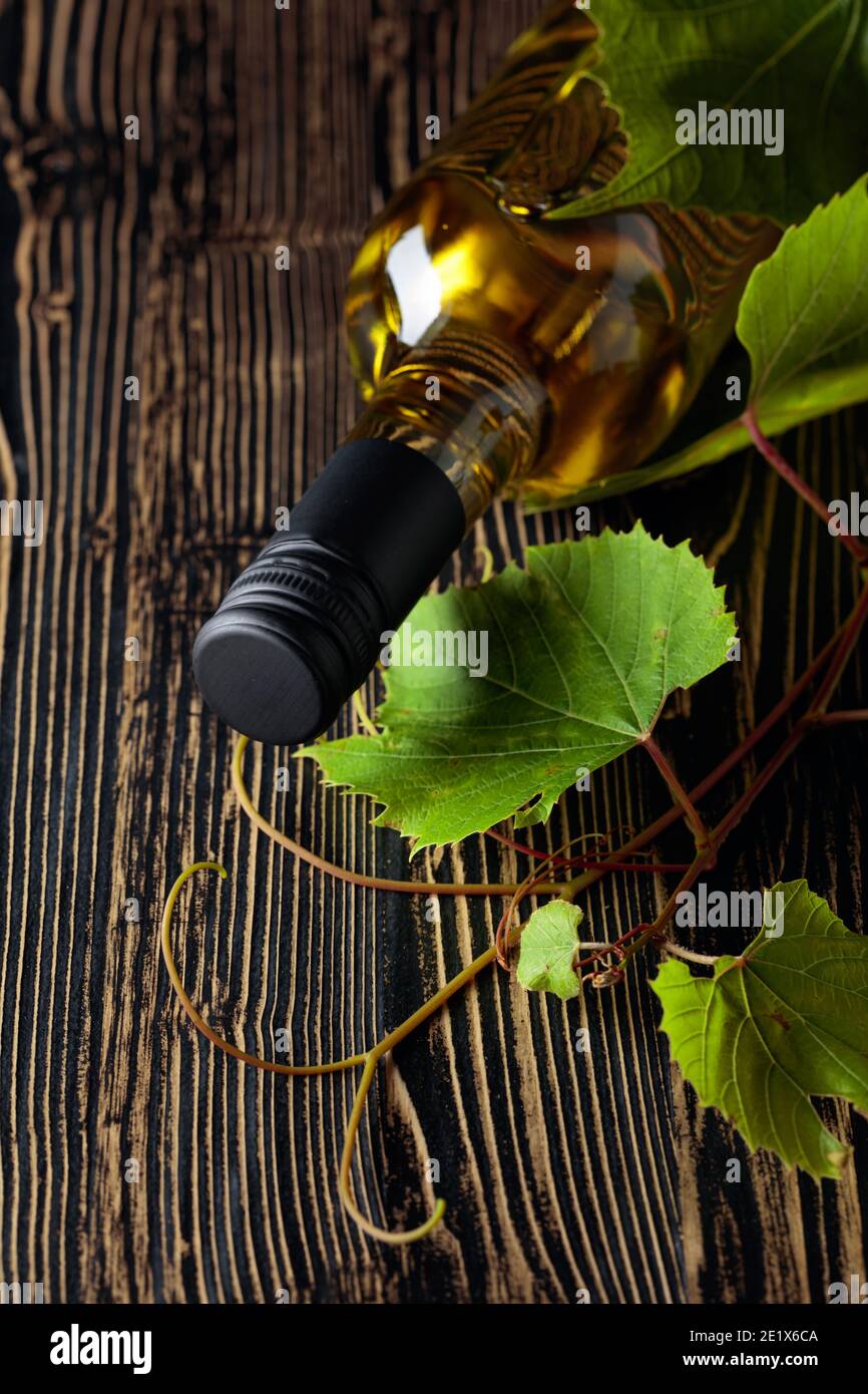An unopened bottle of white wine and grapevine on an old wooden table