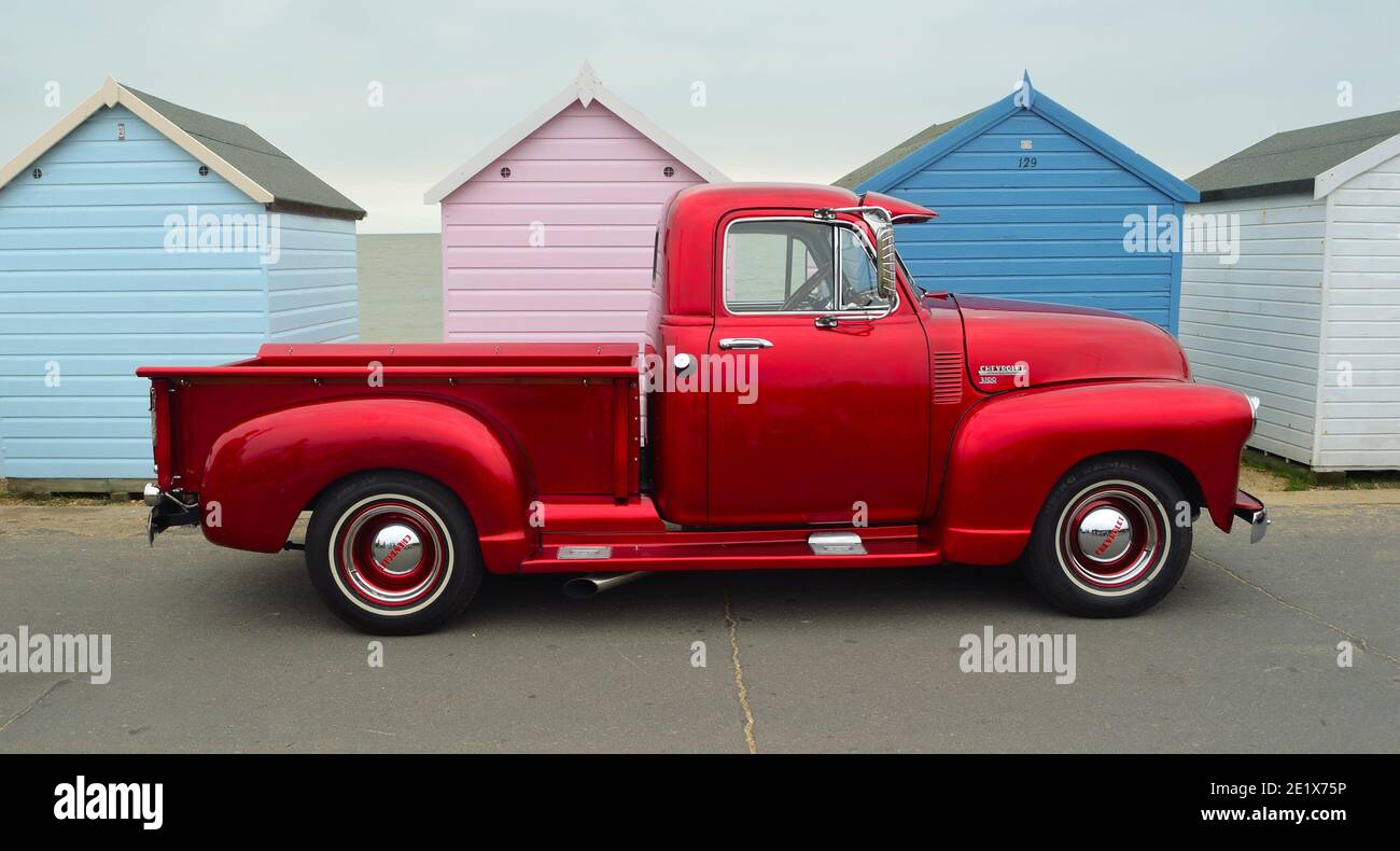 Classic Red  Chevrolet 3100 pickup truck on seafront promenade in front of beach huts. Stock Photo