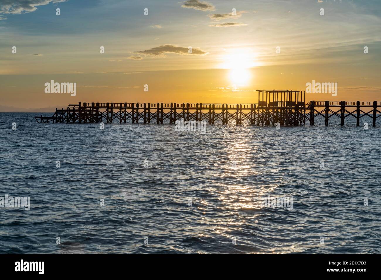 silhouette of a wooden jetty at sunset with blue soft waves in the fore ground Stock Photo