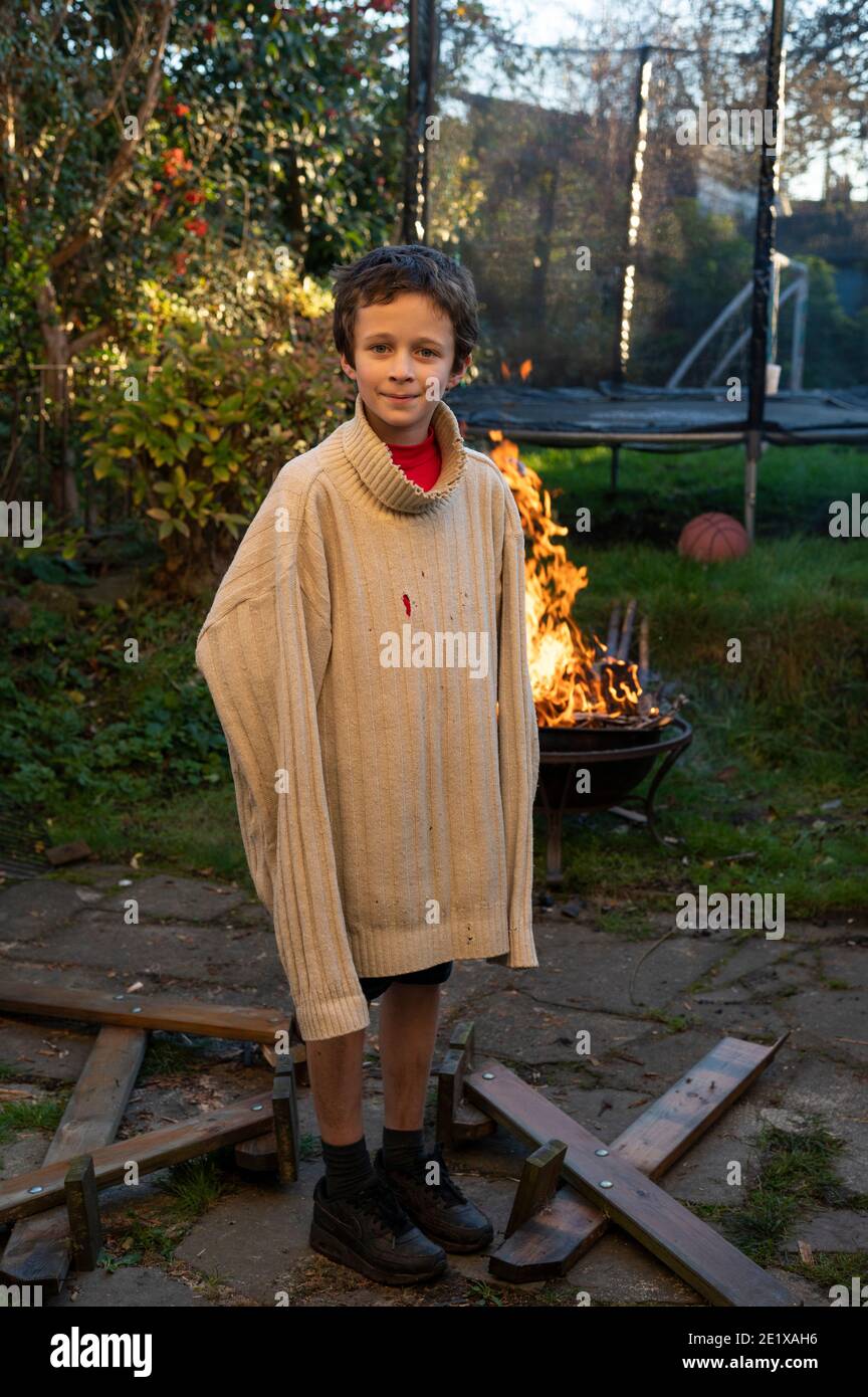 Edinburgh, Scotland, UK. November 2020. A young boy wearing his Dad’s old jumper and playing in the back garden Stock Photo