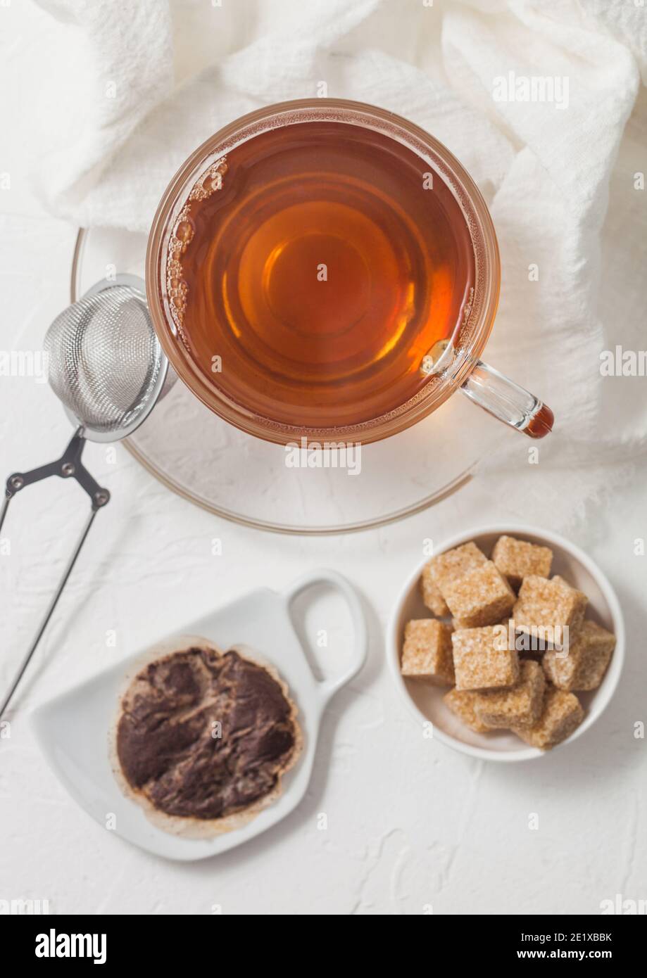 Used teabag on ceramic plate with glass of tea and strainer infuser and cane sugar on white background. Stock Photo