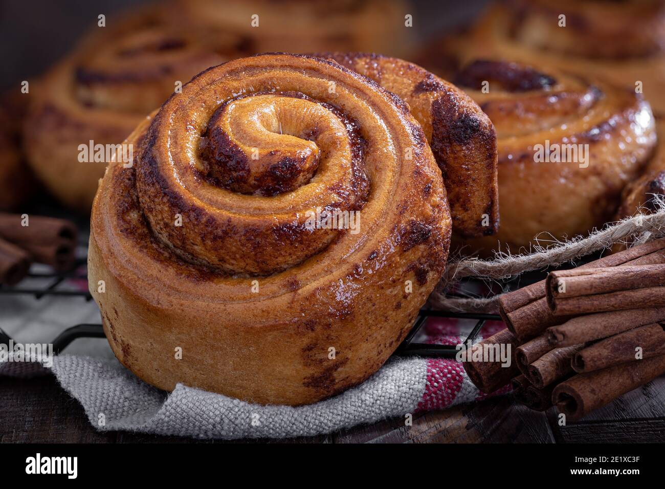 Fresh baked cinnamon buns on a wire rack with cinnamon sticks Stock Photo