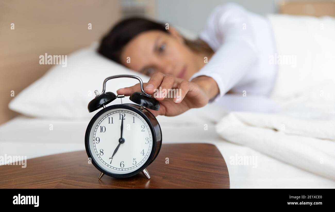 Close up woman turning off alarm clock, woken by signal Stock Photo