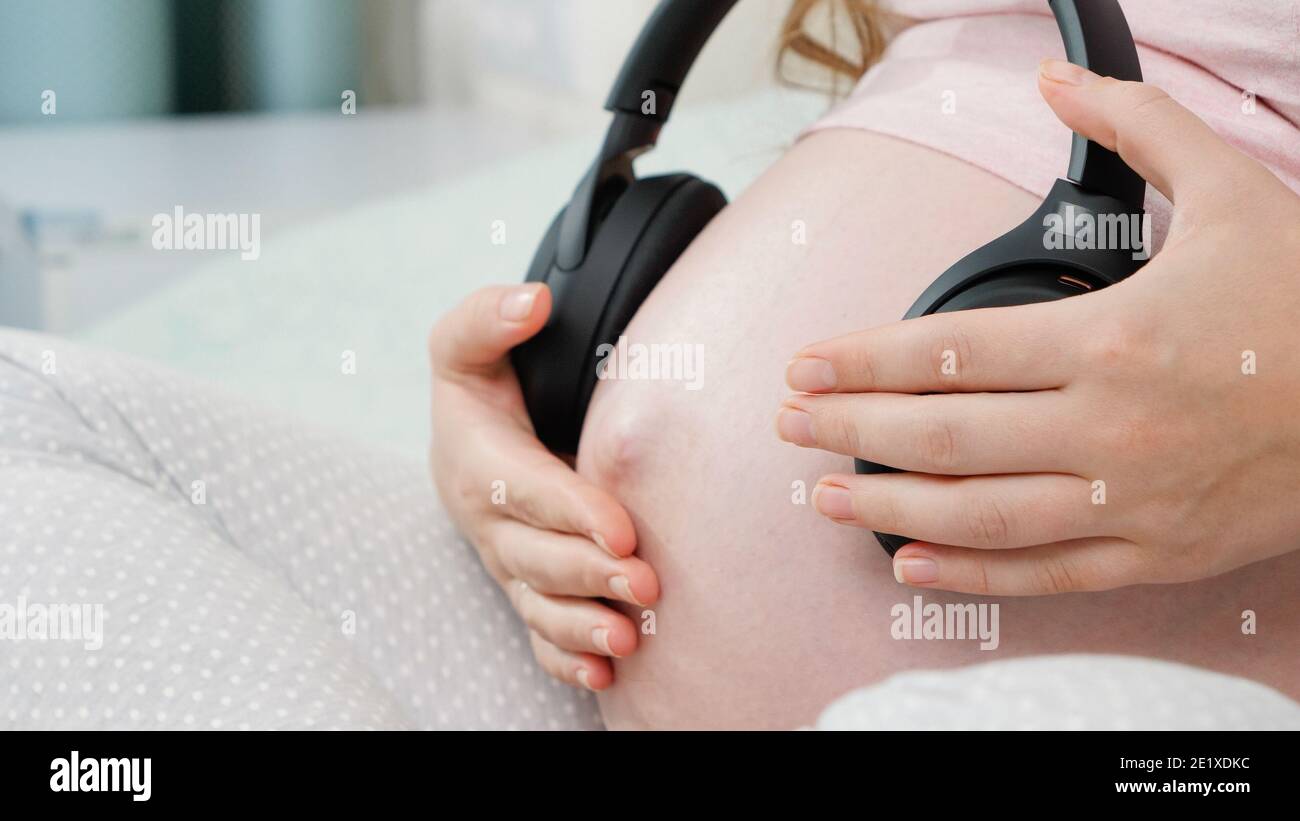 Music and pregnancy. Expectant woman holding headphones near belly