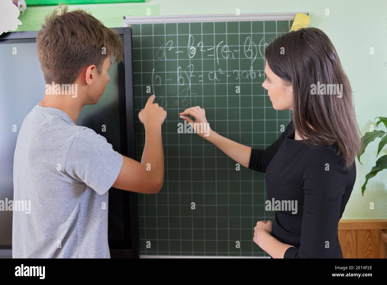 Teenerger Math Male teenager student with teacher near school chalk board at math ...