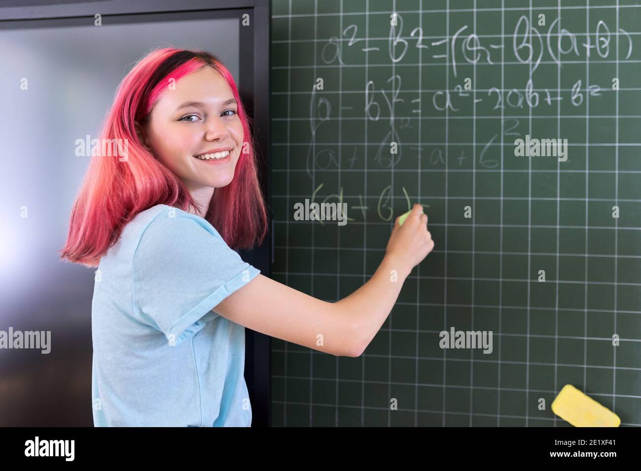 Female student teenager at a math lesson writing in chalk on a blackboard Stock Photo