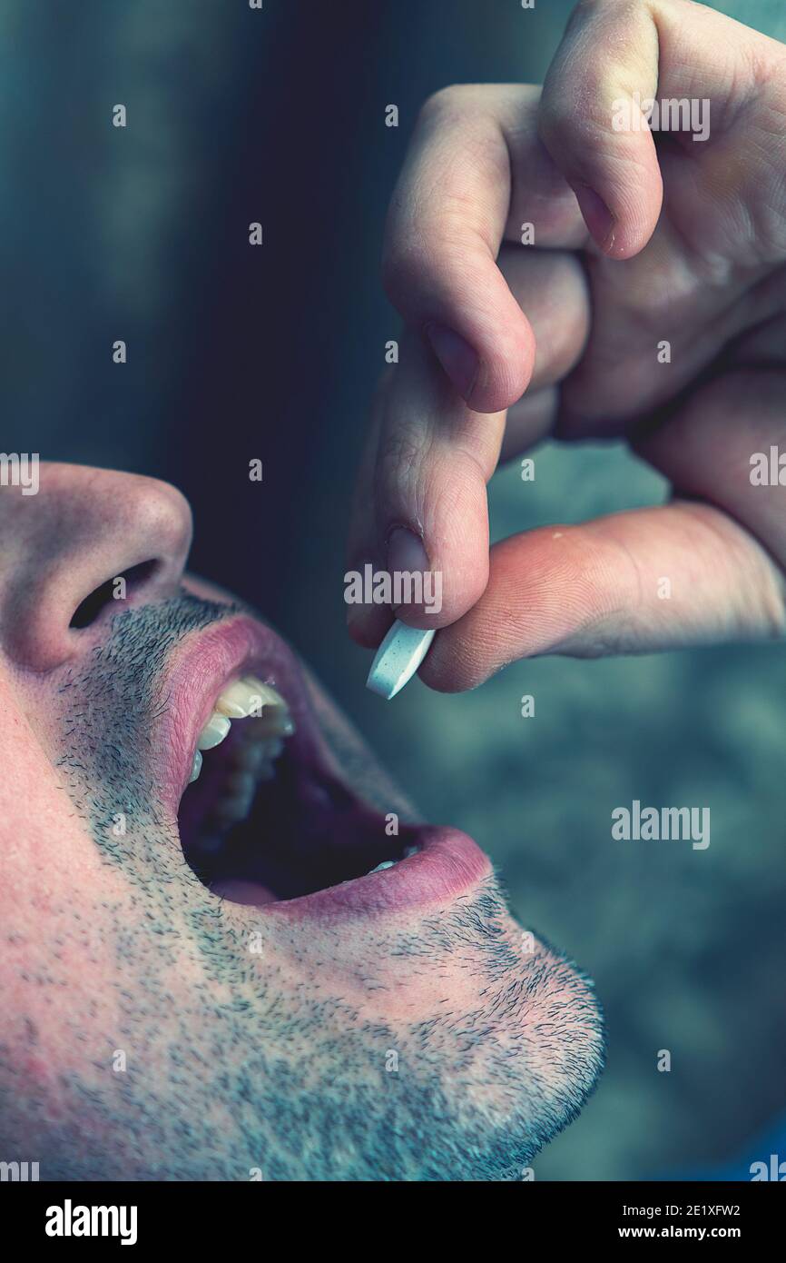 Extreme closeup man face taking white pill, mouth view swallowing pills, illness. man take medicine,open mouth and bring medicine to mouth. toned Stock Photo