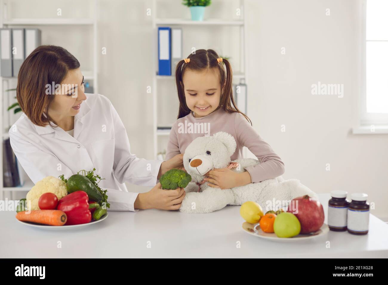 Nutritionist playing with little girl and telling her about benefits of eating healthy food Stock Photo
