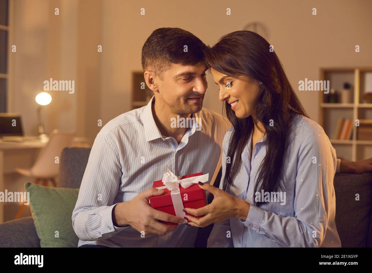 Young man in love tenderly congratulates his girlfriend on Valentine's Day by giving her a gift. Stock Photo