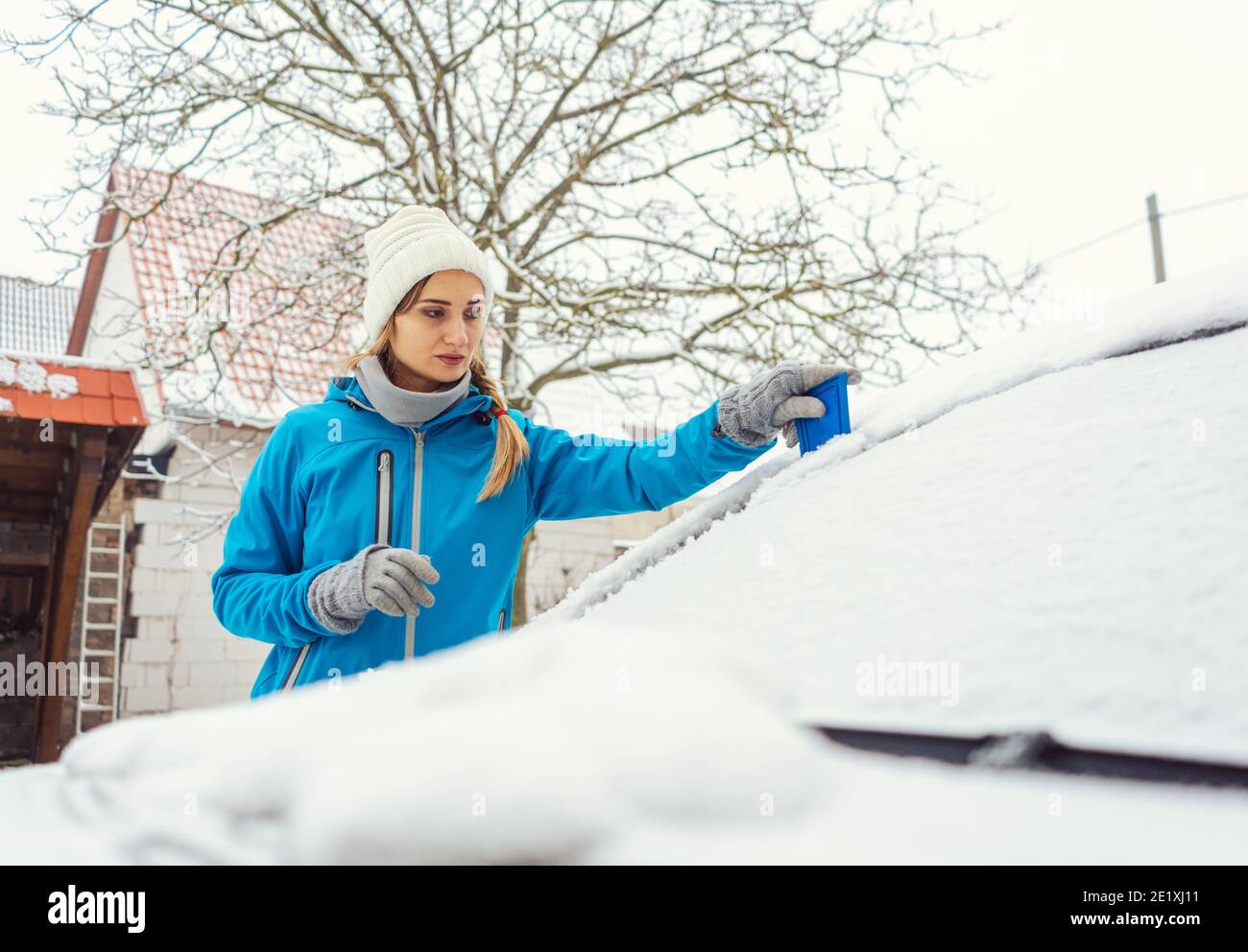 Woman scraping off ice from front window of her car in winter Stock Photo