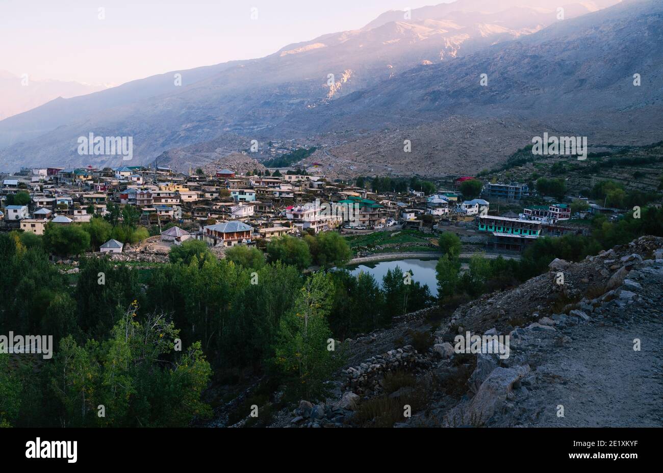 Village flanked by fields, lake, high Himalayan mountains, and trees in the Spiti valley at sunrise in Nako, Himachal Pradesh, India. Stock Photo