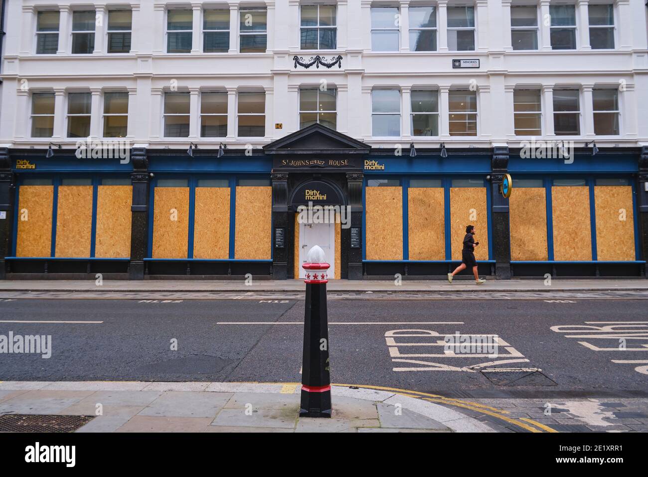 COVID 19 Lockdown - A solitary jogger runs past a closed and boarded Dirty Martini Bar in the City of London during the Coronavirus Lockdown, London, United Kingdom, Sunday 10th January 2021 Stock Photo