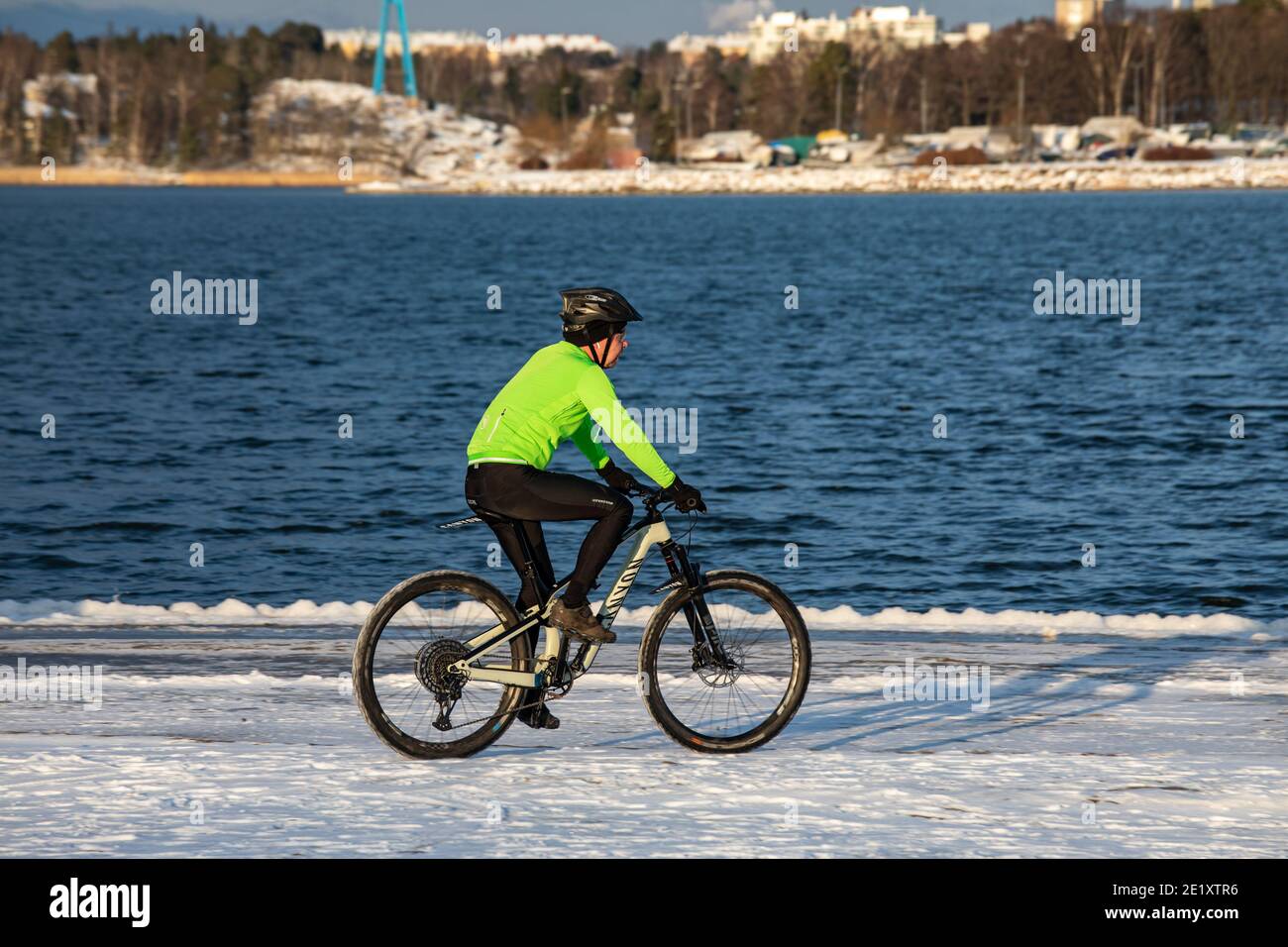 Winter biking. Man with green jacket cycling on snow covered Hietaranta Beach on a sunny winter day in Helsinki, Finland. Stock Photo