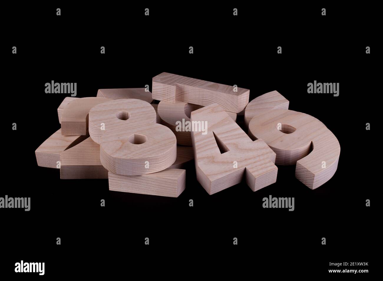 Pile of large random wooden numbers with a black background. Hardwood cutout shapes Stock Photo