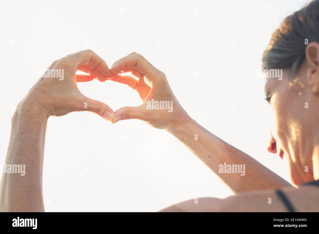 Woman with hands in heart shape on sunny day. Young lady with romantic symbol at twilight. Valentine Day, sunny, healthy lifestyle concepts Stock Photo