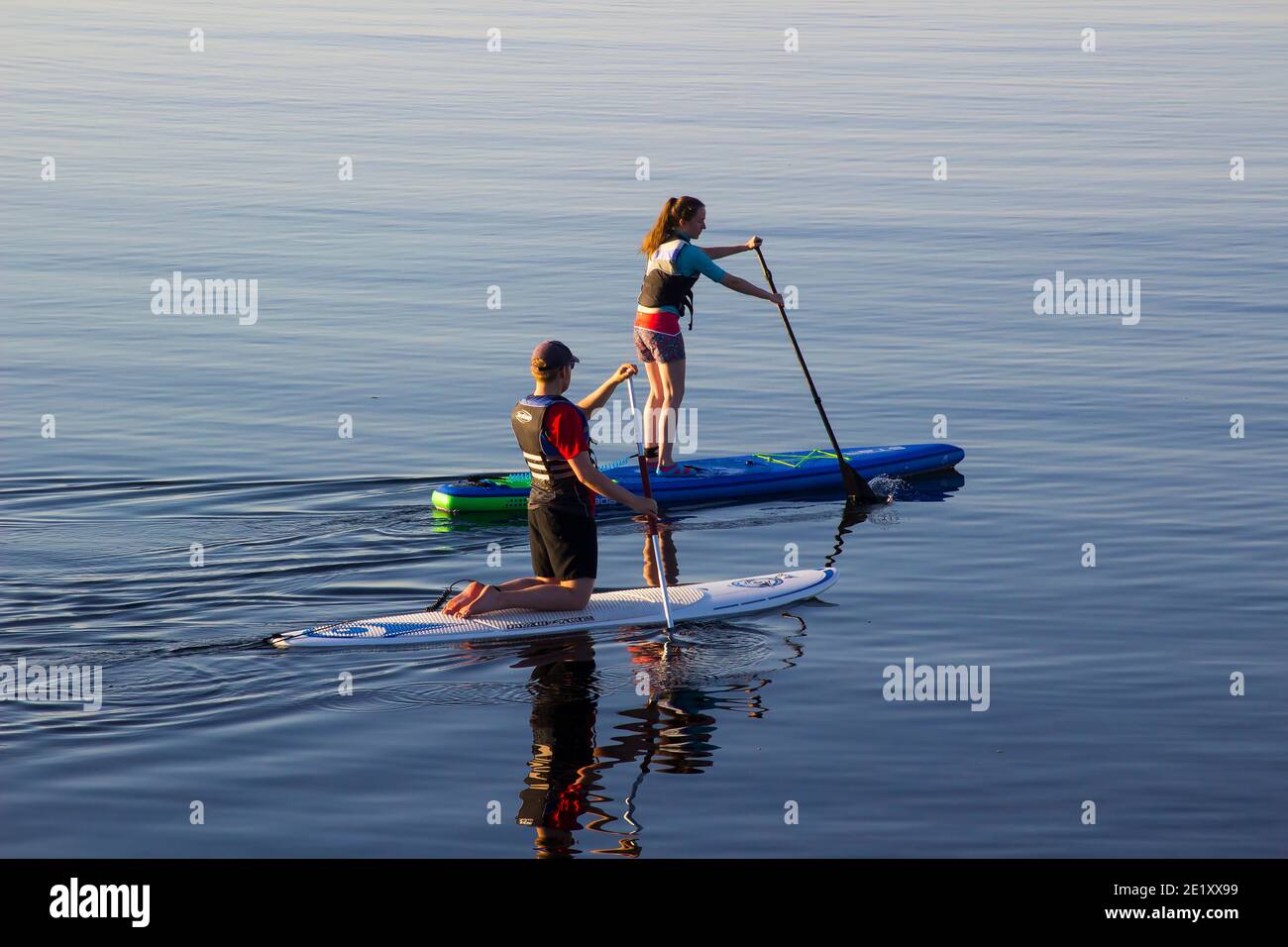 29 June 2018 A couple slowly paddle their surf boards in the calm sea at Groomsport harbour near Bangor Northern Ireland on a calm and warm summer eve Stock Photo