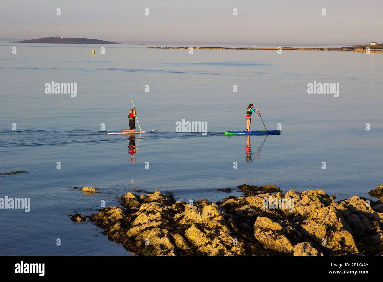 29 June 2018 A couple slowly paddle their surf boards in the calm sea at Groomsport harbour near Bangor Northern Ireland on a calm and warm summer eve Stock Photo