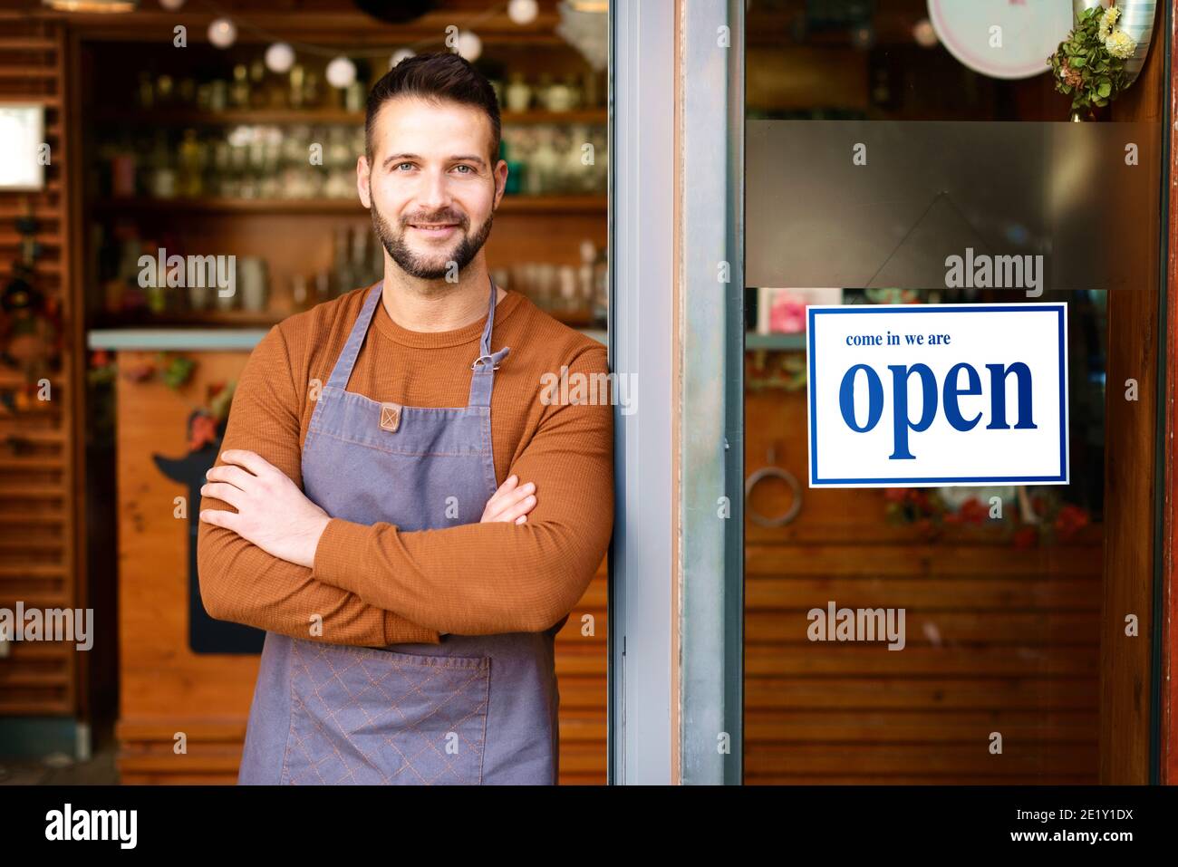 Portrait of smiling owner man standing at his cafe door with open