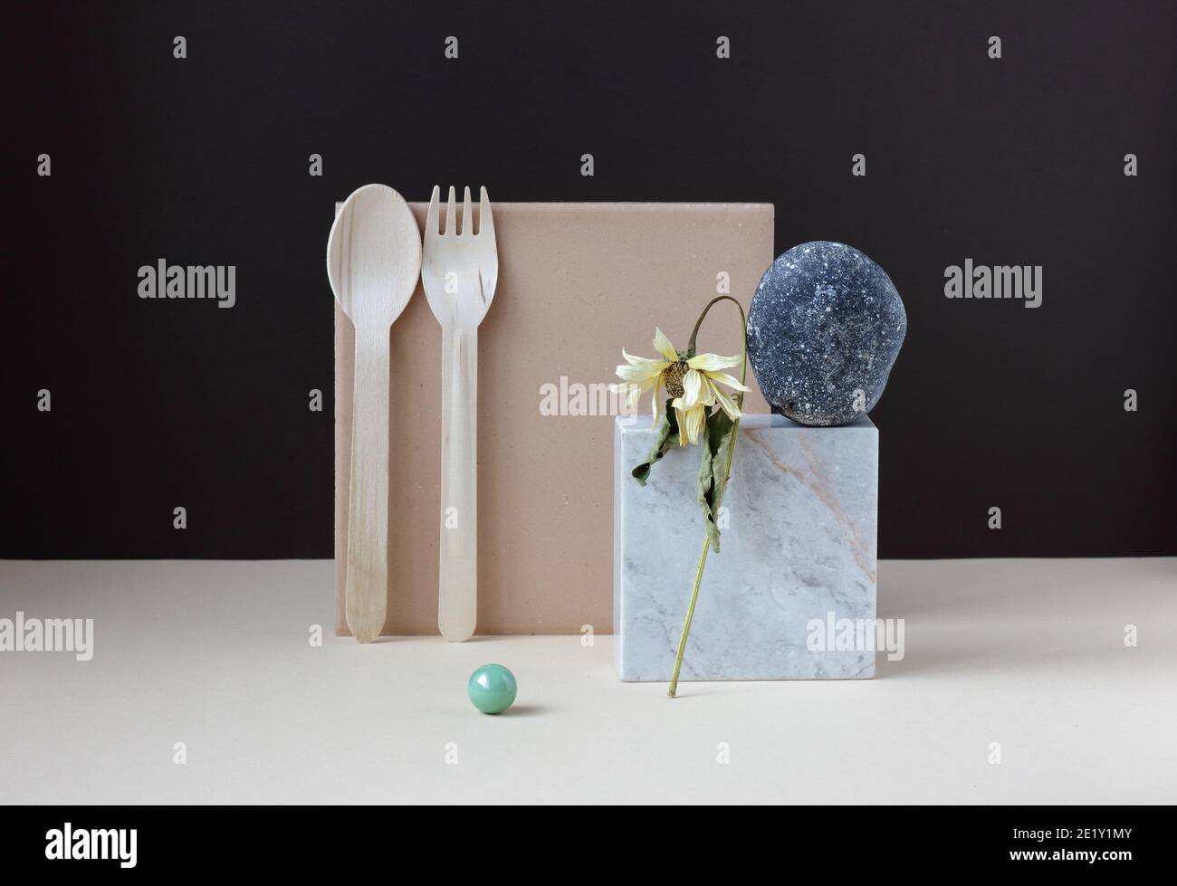 Simple geometric minimalism still life with dried flower balancing upon marble and stone  and disposable wooden zero waste dinnerware on beige table o Stock Photo