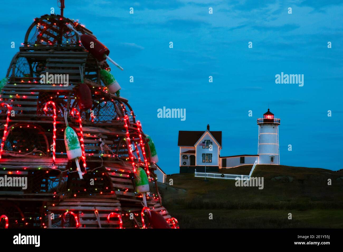 Nubble lighthouse is lit up for the holidays in Maine with traditional wooden lobster trap holiday tree in the forground. A New England tradition. Stock Photo
