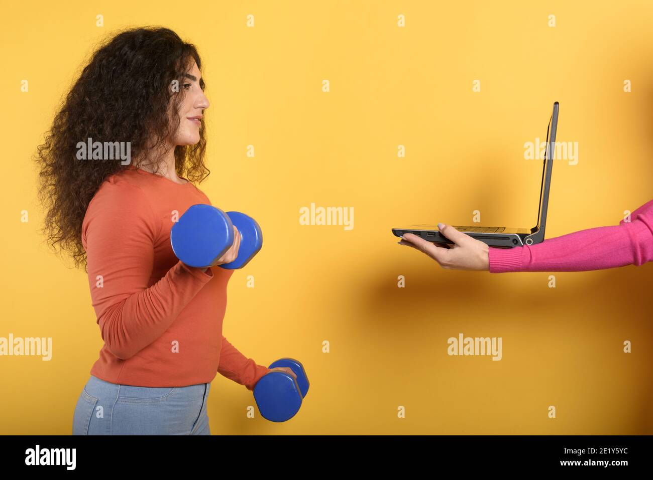 Girl with handlebars ready to start the gym online with a computer. yellow background Stock Photo