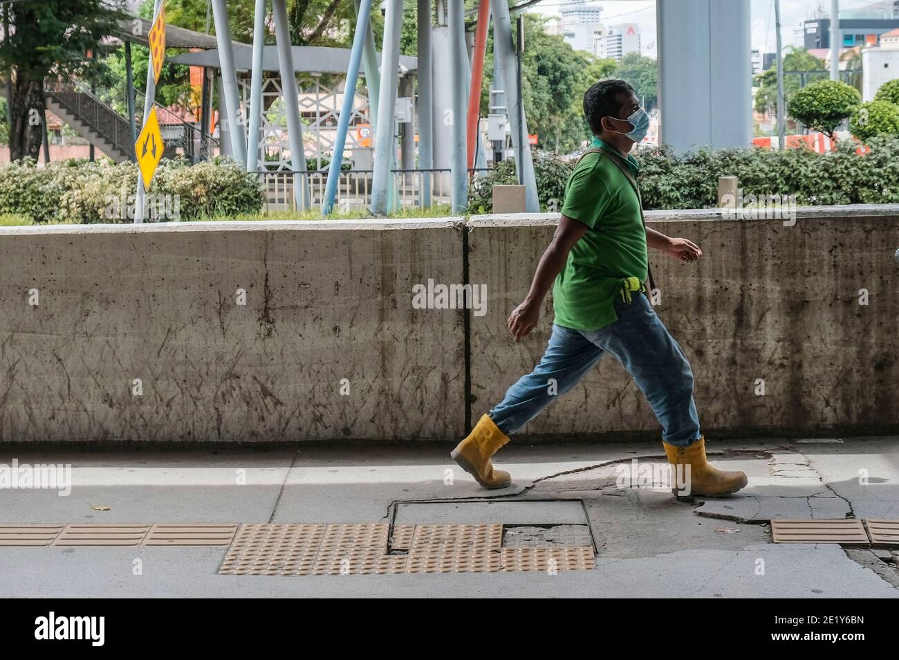 A foreign worker wearing a face mask as a precaution against the spread of Covid-19 walks on the street in Kuala Lumpur. Stock Photo
