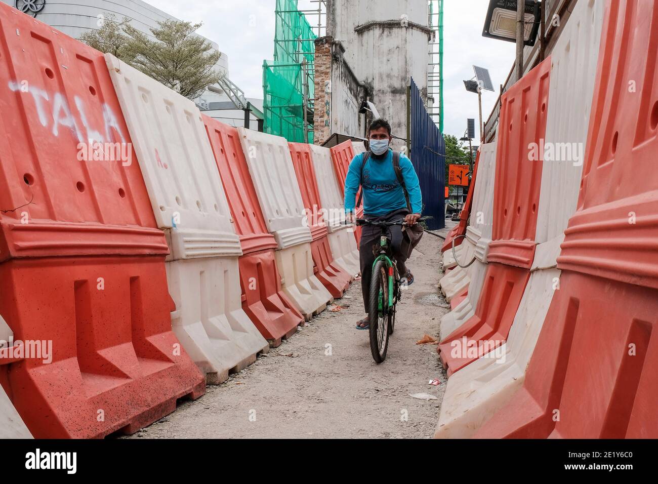 A foreign worker wearing a face mask as a precaution against the spread of Covid-19 rides a bike through barricades in Kuala Lumpur. Stock Photo