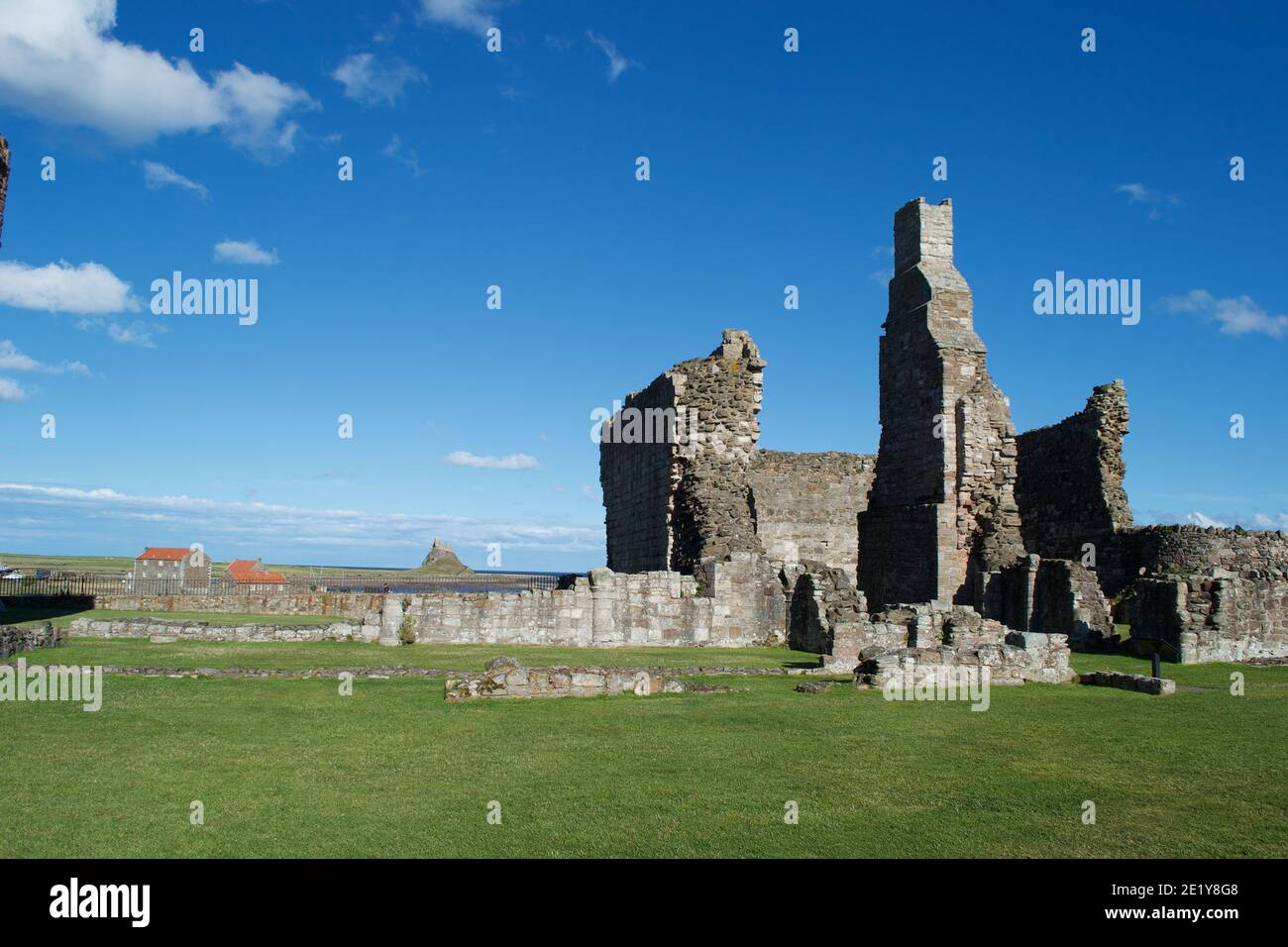 Ruins of a large stone building by the coast on a sunny day. Tall chimney stack still standing amongst crumbling walls on the green grass lawn, beneat Stock Photo