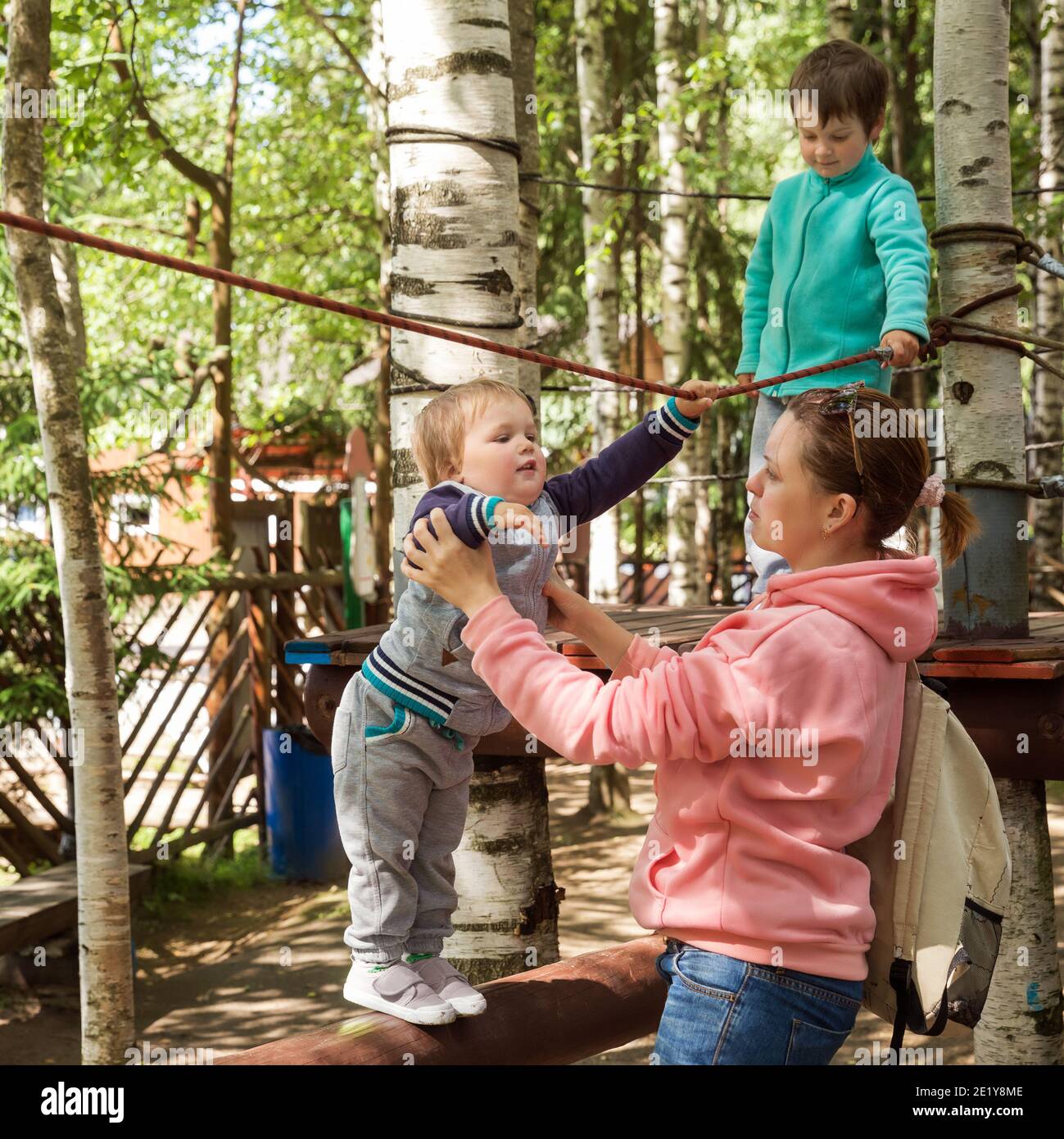 Family with children in the amusement park. Mom helps the baby stay on the obstacle course Stock Photo