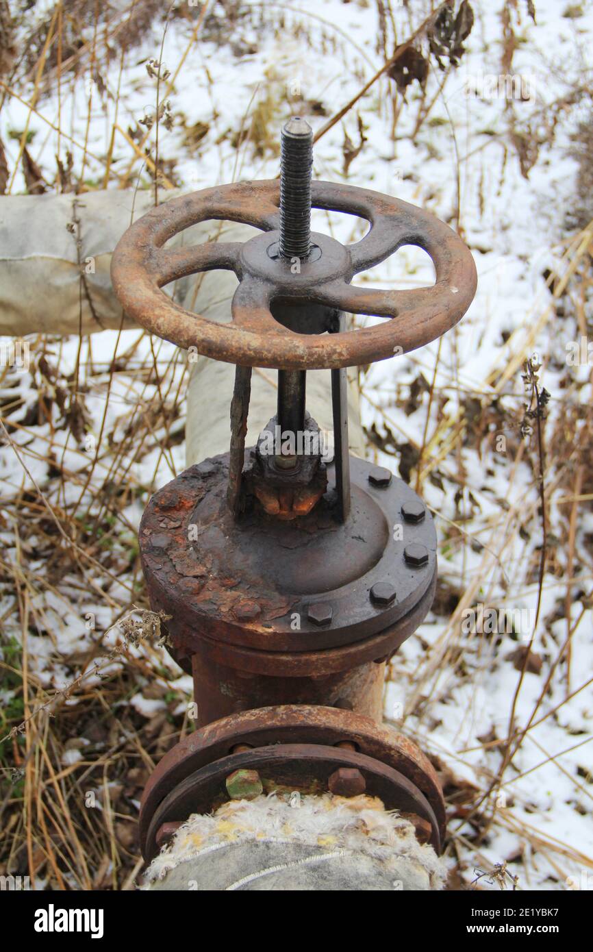 Old damaged and rusty iron oil pipe valve wheel. Metal, pipeline and mechanic concept. An old iron valve on a gas pipe. A valve to cover the pipe with a round handle. Stock Photo
