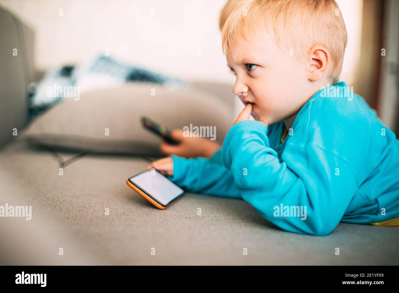 Little Caucasian Boy Playing Games On Phone Thoughtfully Stock Photo