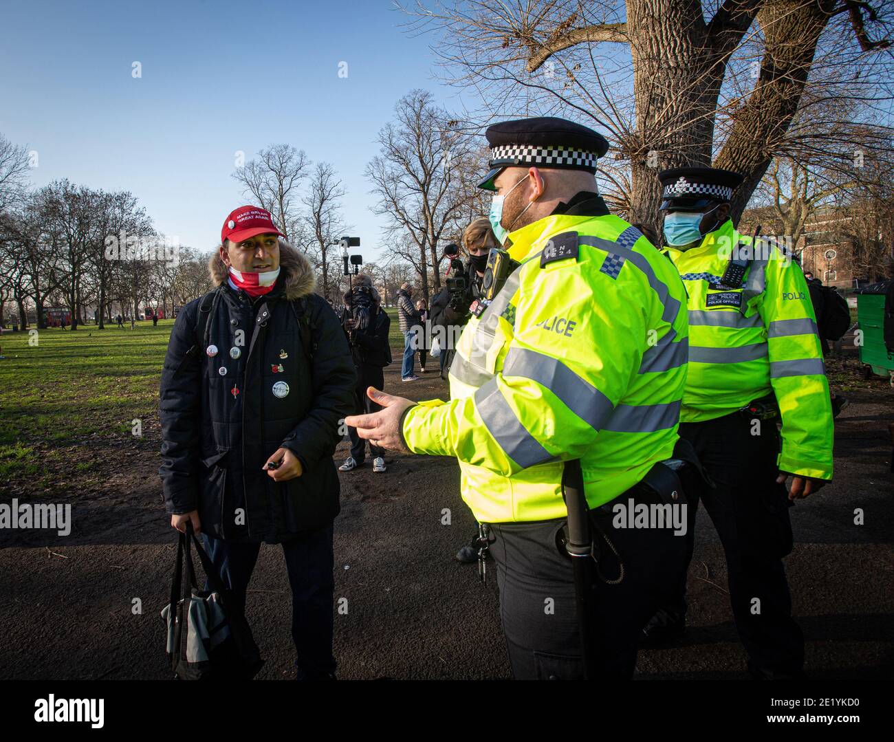 A protester wearing a 'Make Britain Great Again' baseball cap is questioned by Police on Clapham Common park during the anti-lockdown demonstration. Stock Photo