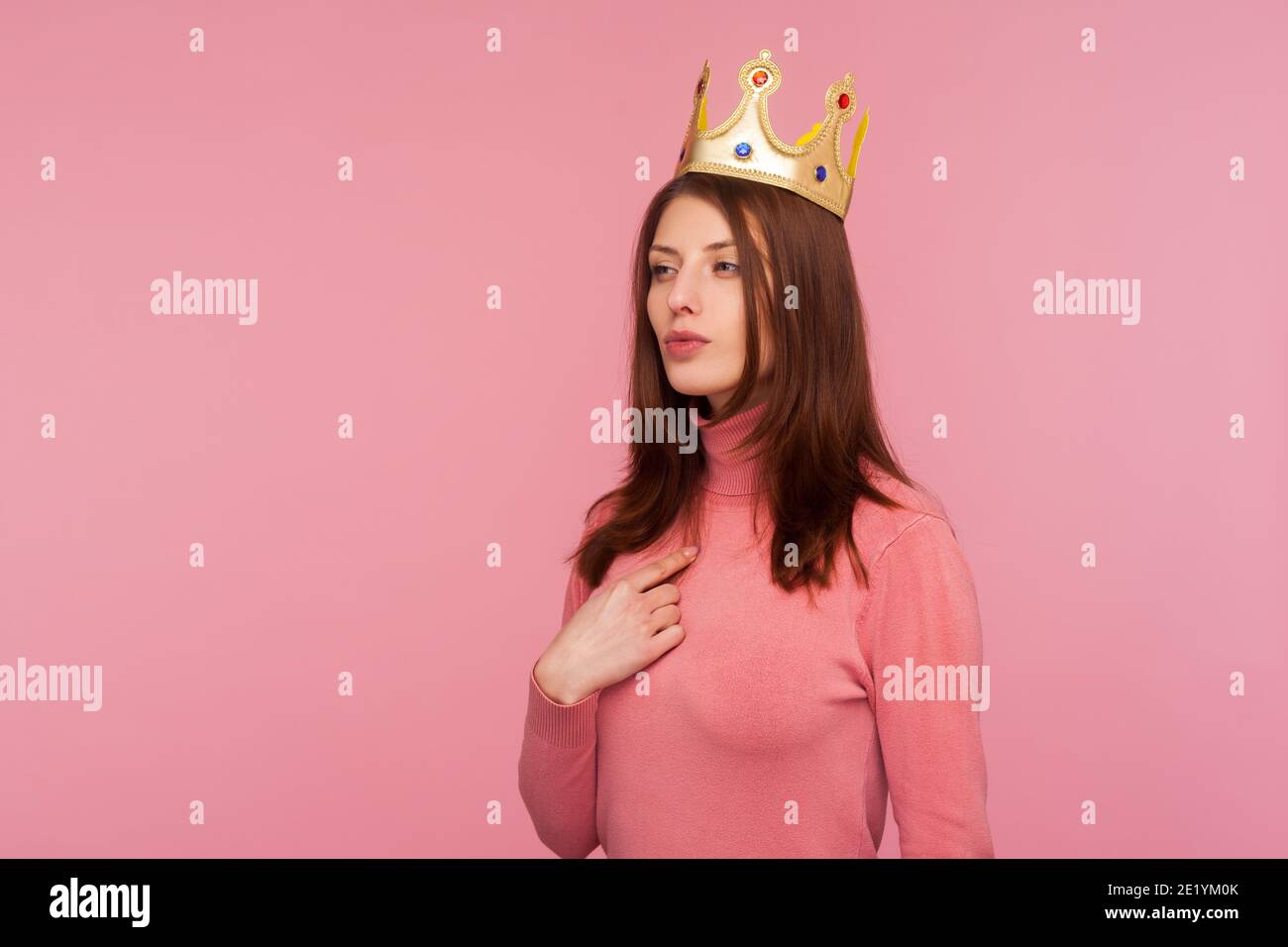Ambitious self-confident authoritative woman wearing crown on head and pointing finger at herself, looking with arrogance. Indoor studio shot isolated Stock Photo