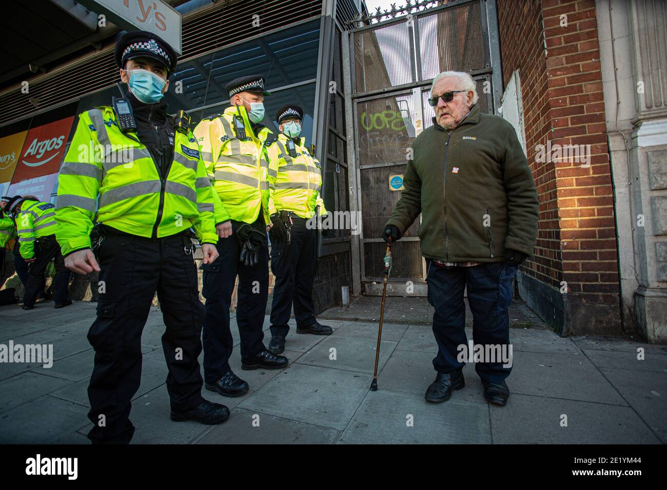 Pensioner protester with walking stick is  standing in front of Police on Clapham High Street during the anti-lockdown demonstration on January 9, 202 Stock Photo