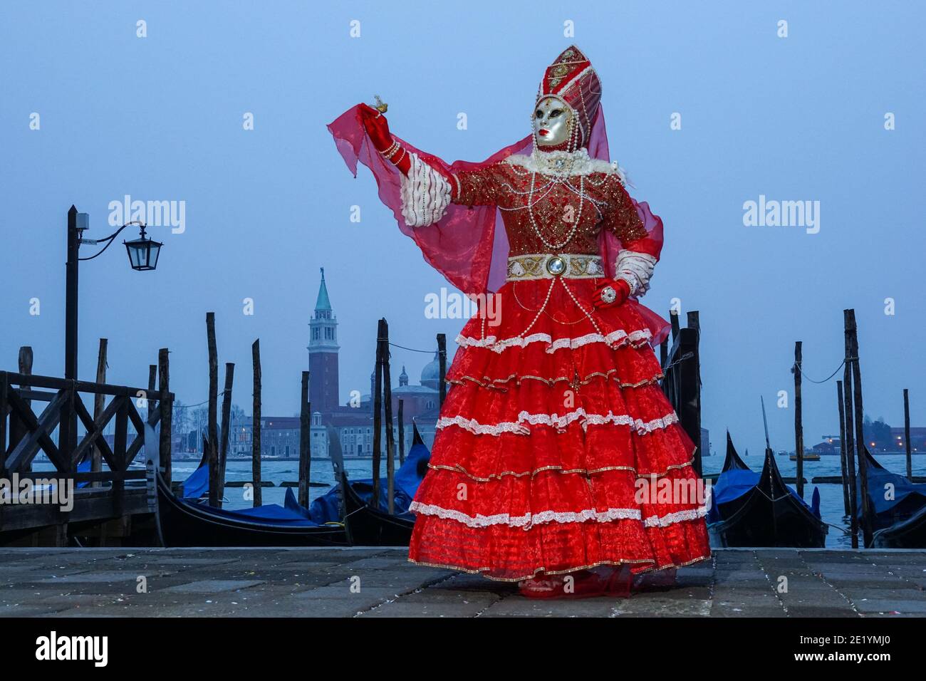 Woman dressed in traditional decorated costume and mask during the Venice Carnival with the San Giorgio Monastery in the background Venice, Italy Stock Photo