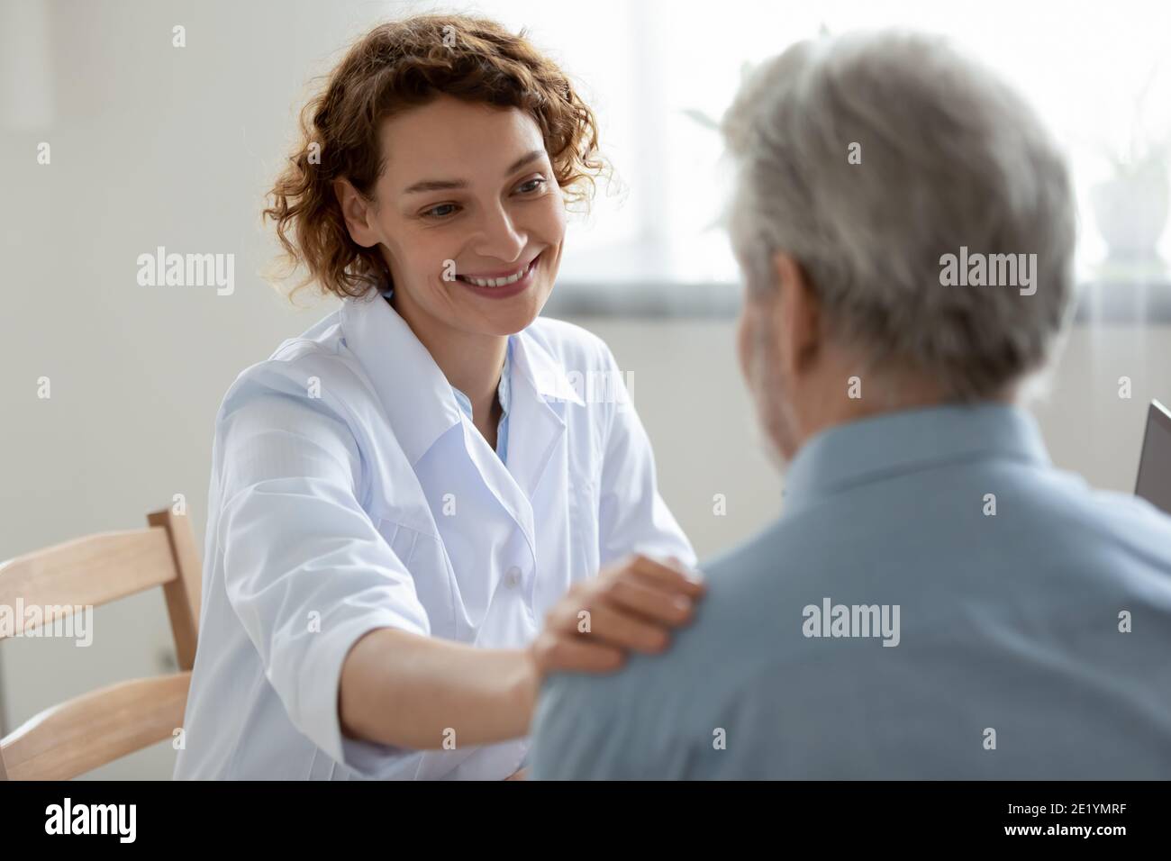 Happy young 30s physician doctor supporting elderly patient. Stock Photo