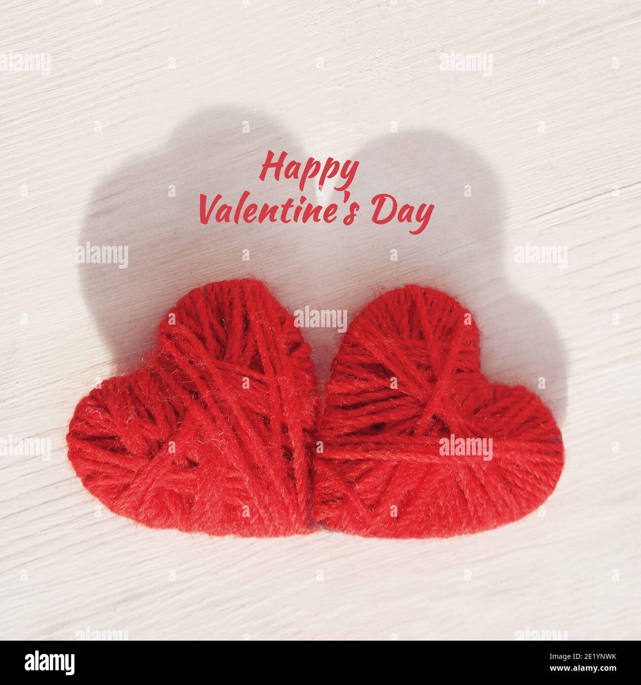 Two red hearts handmade from wool threads on a wooden light background ...