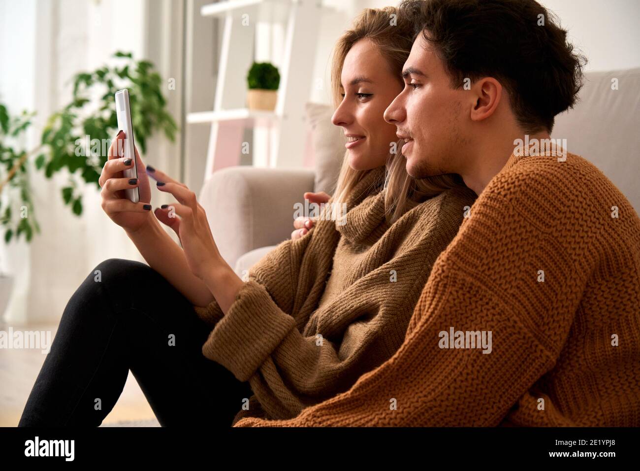 Young happy couple customers holding smartphone using mobile cell phone at home. Stock Photo