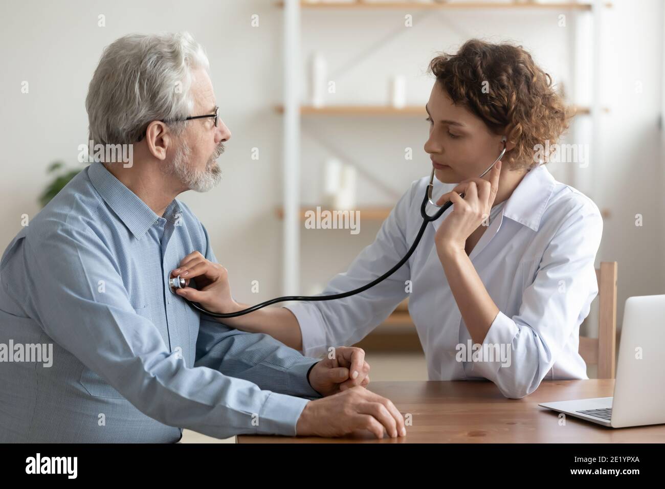Focused young female cardiologist listening heartbeat of old patient. Stock Photo