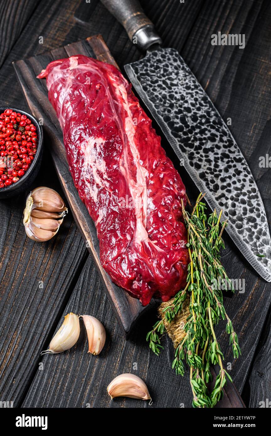 Raw Onglet Hanging Tender beef meat steak on a wooden cutting board. Black wooden background. Top view Stock Photo