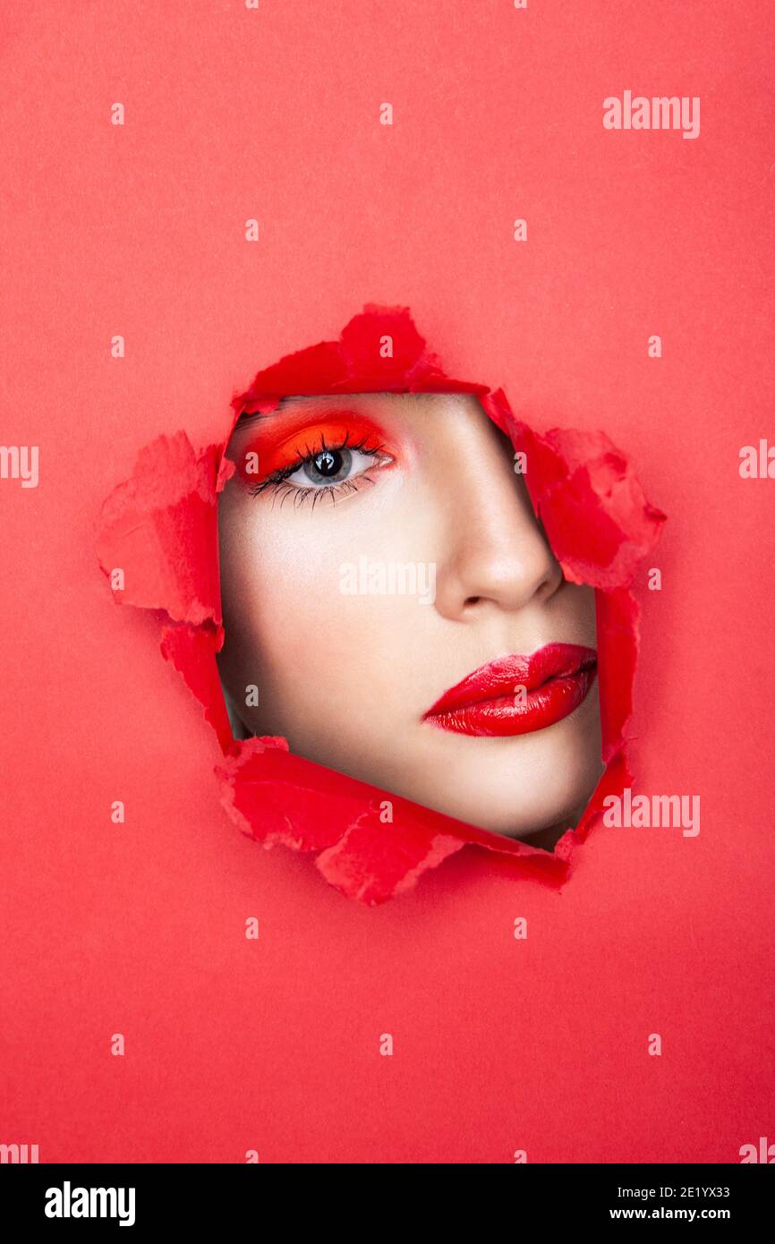 Woman with red visage looking through torn paper Stock Photo