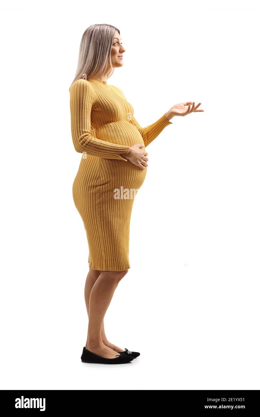 Full length shot of a pregnant woman in a yellow dress holding her belly and gesturing with hand isolated on white background Stock Photo