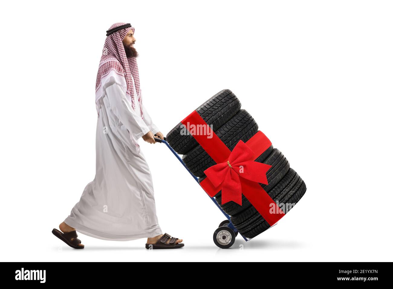 Full length profile shot of a saudi arab man in traditional clothes pushing a hand truck with a tires isolated on white background Stock Photo