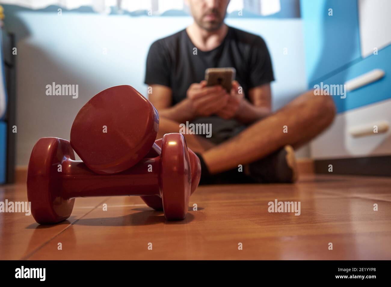 Man with weights and mobile phone in his hands, sports at home, selective focus Stock Photo