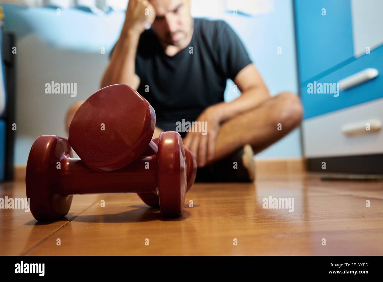 Man in his bedroom ready to do sport with weights, depressed or thinking state, selective approach Stock Photo