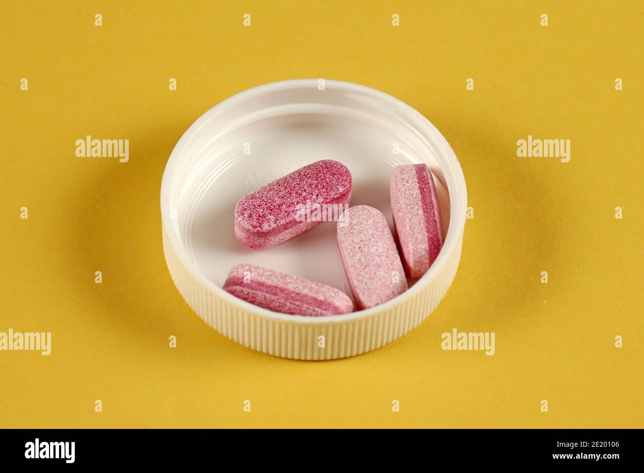 Pink health multivitamin supplement tablets inside white plastic lid Stock Photo